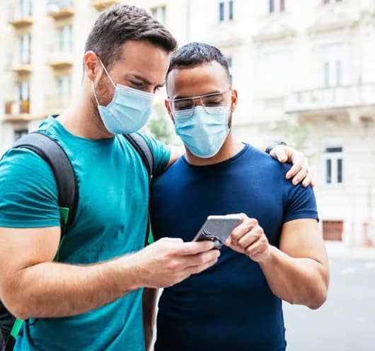 Two guys glancing at a mobile phone while they are both wearing masks